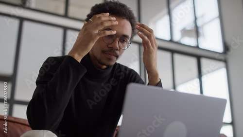 Stressed man holding head over laptop