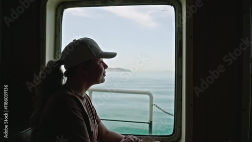 Wallpaper Mural Caucasian woman in cap gazes out ferry window, serene ocean view beyond. Female reflects, calm sea voyage, travel peace. Journey moment, maritime transportation, personal time on water. Torontodigital.ca