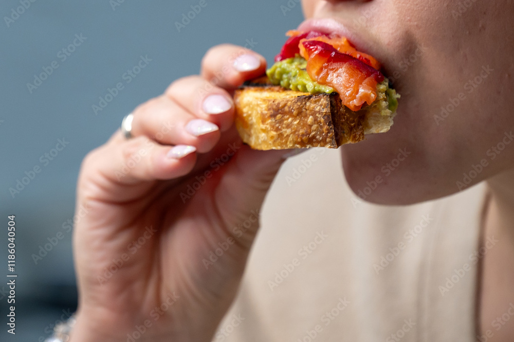 A close-up of a person enjoying a slice of toasted bread topped with avocado, smoked salmon, and colorful vegetables. The focus is on the vibrant toppings and the act of eating. A close-up of a person enjoying a slice of toasted bread topped with avocado, smoked salmon, and colorful vegetables. The focus is on the vibrant toppings and the act of eating.