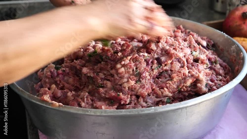Person is making meatballs in a bowl. The meatballs are being mixed and shaped by the person's hands