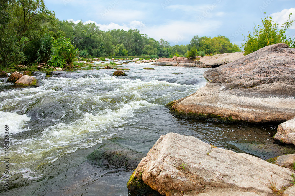 Serene river flowing through rocky terrain under a cloudy sky in the wilderness