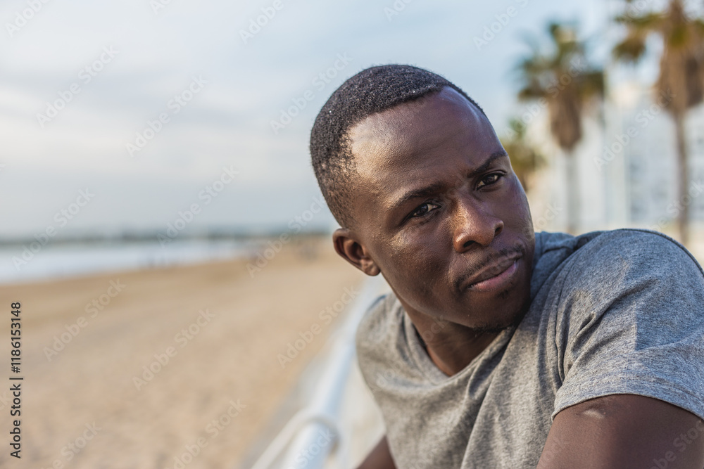 Fototapeta premium Portrait of young black man with sunset sky and palm trees on the promenade in the background