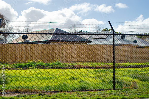  a chain-link fence with barbed wire as a barrier with some Australian suburban houses behind, to deter people from entering the property, providing privacy and safety protection for the residents. photo