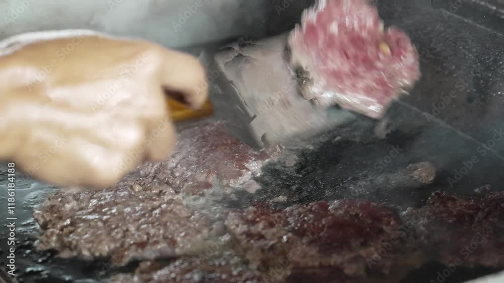 A chef flips a burger patty on a hot flat griddle