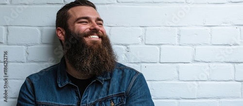 Happy bearded man smiling joyfully in a close-up shot against a textured white brick wall, featuring ample negative space for text placement. photo