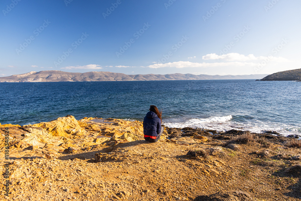 Woman standing alone on the cliffs from an island in the middle of the sea. Concept image for solitude and loneliness. Woman photographed from behind.
