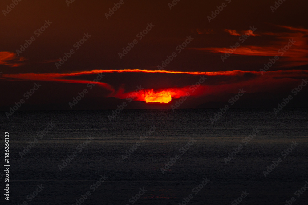 Spectacular sunset clouds on sky above Mediterranean Sea in Greece. Seaside sunset landscape photo with mountains in background.