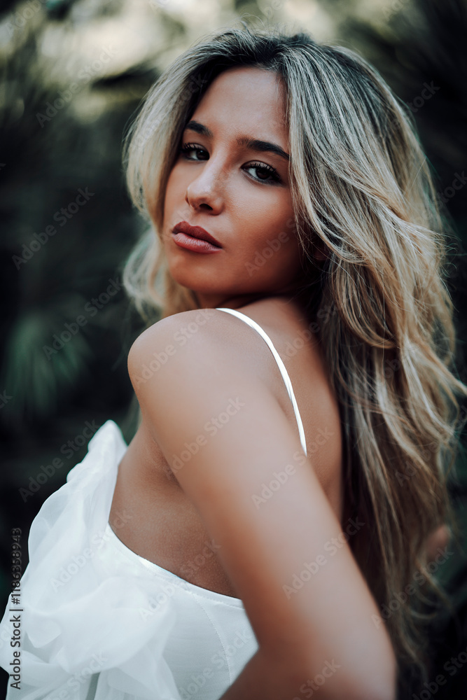 Chica rubia joven posando en jardin con traje blanco