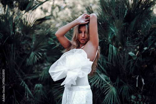 Chica rubia joven posando en jardin con traje blanco