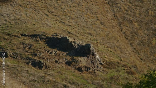 Rocky hillside with sparse vegetation under sunlight. Dry terrain and geological formations in a natural landscape.