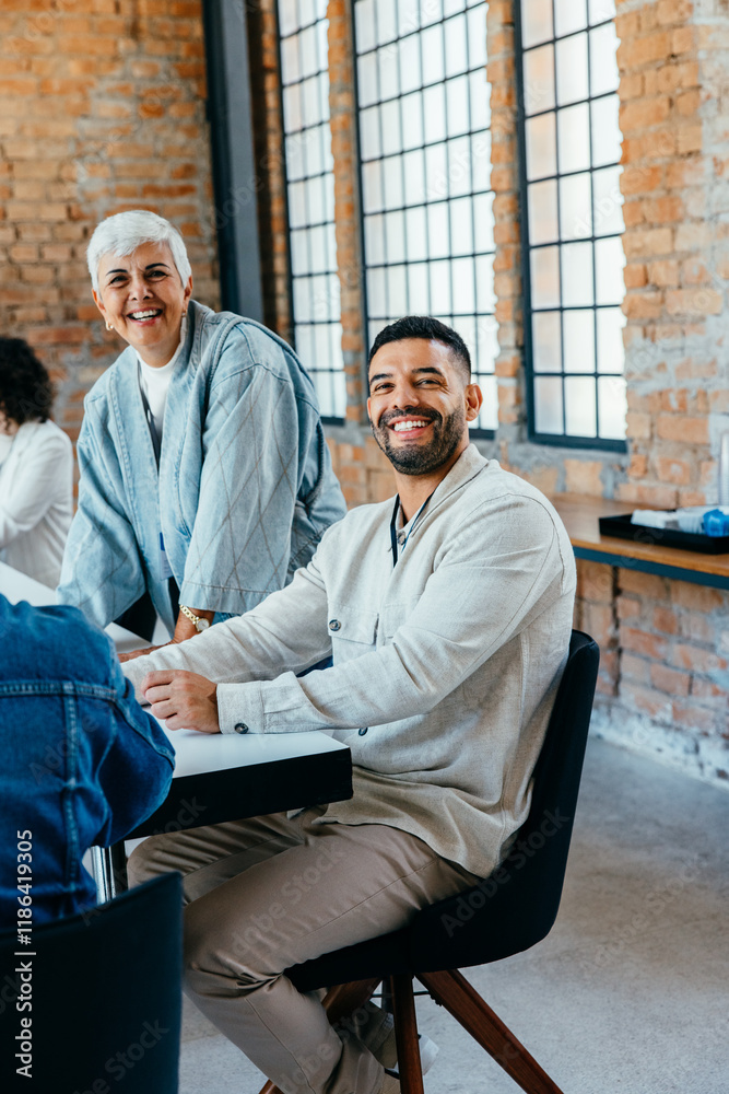Fototapeta premium Diverse age range of colleagues engaged in a friendly meeting in a bright, modern office with exposed brick and large windows