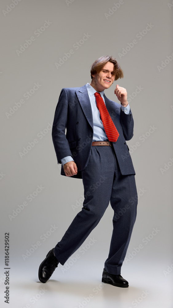 Full-length portrait of young business man, dressed blue formal suit and red tie, dancing expressing joy and happiness against grey background. Concept of human emotions, self-expression. Ad Full-length portrait of young business man, dressed blue formal suit and red tie, dancing expressing joy and happiness against grey background. Concept of human emotions, self-expression. Ad