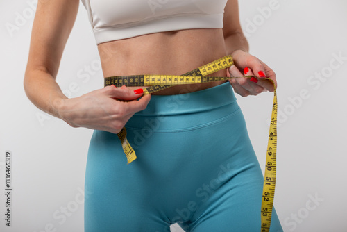 Beautiful slim healthy woman fitness lady measuring waist with yellow measuring tape on grey background