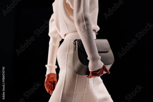 Female figure dressed in classic long set white skirt and sweater, woman holding gray handbag