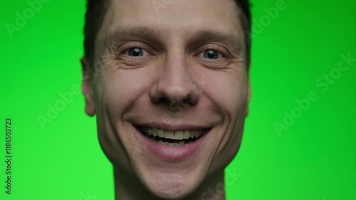 A young man smiles warmly, his laugh lines visible, expressing genuine happiness. Portrait of a cheerful male on a green chroma key background. photo