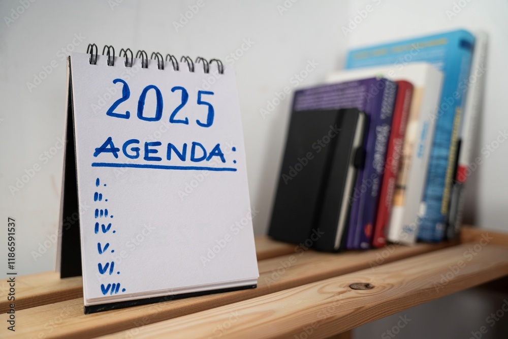 otwarty notes na półce z kartką na której zapisany jest tekst: 2025 Agenda oraz poniżej wykropkowane miejsce na tekst