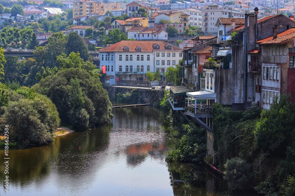 A European townscape with a river flowing through it, featuring old buildings with red rooftops and lush green trees. Amarante, Portugal. A European townscape with a river flowing through it, featuring old buildings with red rooftops and lush green trees. Amarante, Portugal.