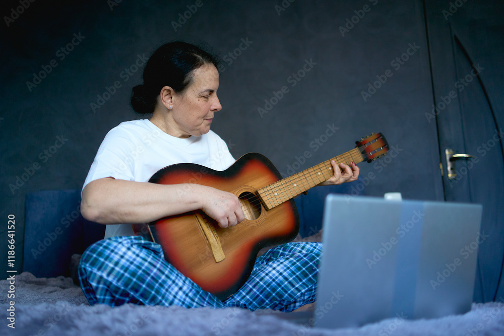 Obraz premium a senior woman learns to play the guitar with online lessons