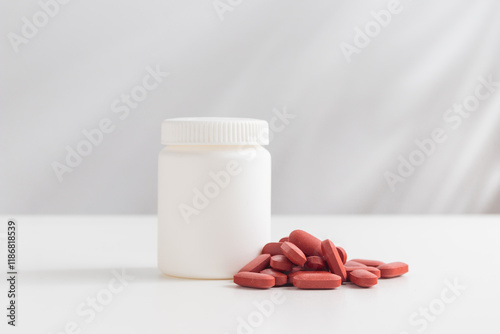 Red pills and plastic medicine bottle on a white background with copy space. Medicine and health concepts include a jar with Ferrum or iron pills or vitamin Fe. High-quality photo mock-up