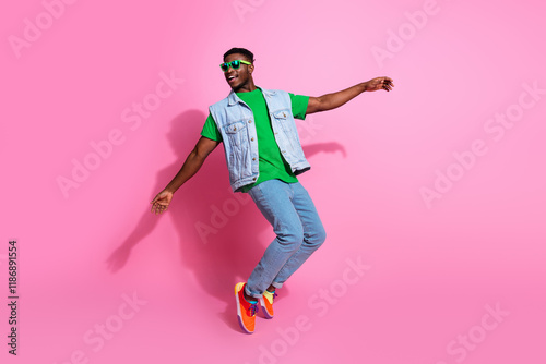 Vibrant young man with black hair and trendy denim outfit exudes happiness against a lively pink background.