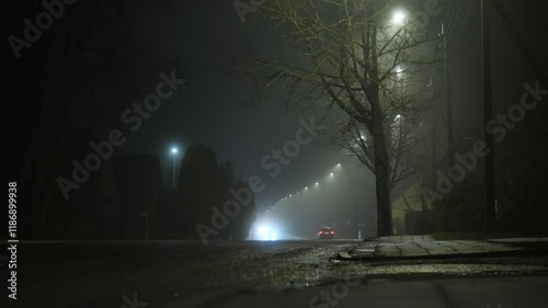 Small, misty road at night with headlights cutting through the fog.