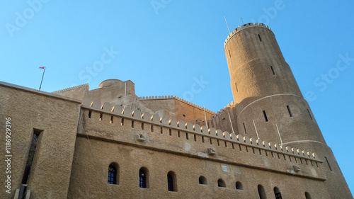 Fort Al-Jalali in Muscat, Oman, A stunning view of a historic fort with a prominent cylindrical tower, featuring traditional architecture and a flag against a clear blue sky.