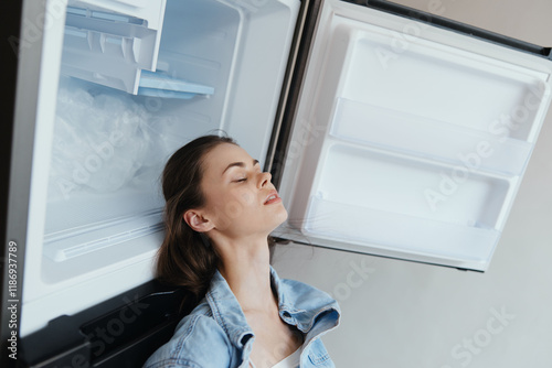 A young woman resting her head against an open refrigerator, seeking relief from heat, wearing casual clothing, conveying a feeling of contentment in a modern kitchen Free Download A young woman resting her head against an open refrigerator, seeking relief from heat, wearing casual clothing, conveying a feeling of contentment in a modern kitchen - GFXLoad