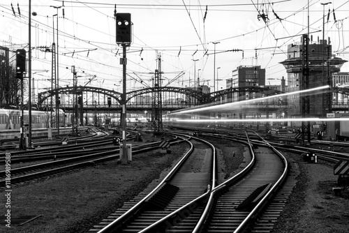 Fast train arriving at Munich main station (Germany) in the evening. Blurred light traces. Railway infrastructure, signals, glistening tracks, switches. Long exposure in black and white (greyscale).