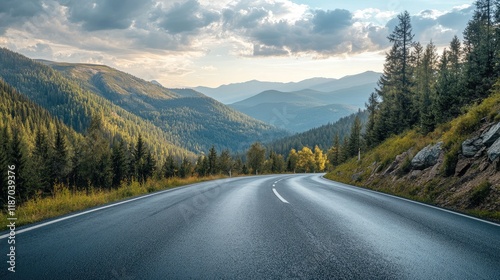 Winding asphalt road through lush green mountains and forest under a dramatic cloudy sky in a serene landscape setting photo