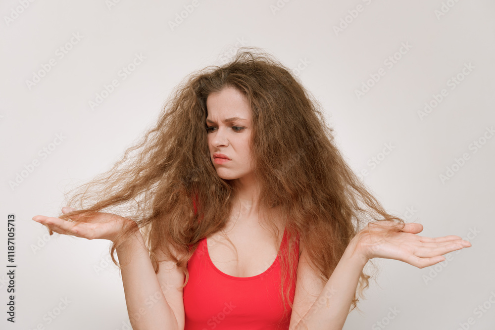 A young woman with voluminous, curly hair looks frustrated as she examines her dry, tangled strands.The struggle of maintaining unruly hair, highlighting beauty challenges and self-care. Bad hair day A young woman with voluminous, curly hair looks frustrated as she examines her dry, tangled strands.The struggle of maintaining unruly hair, highlighting beauty challenges and self-care. Bad hair day