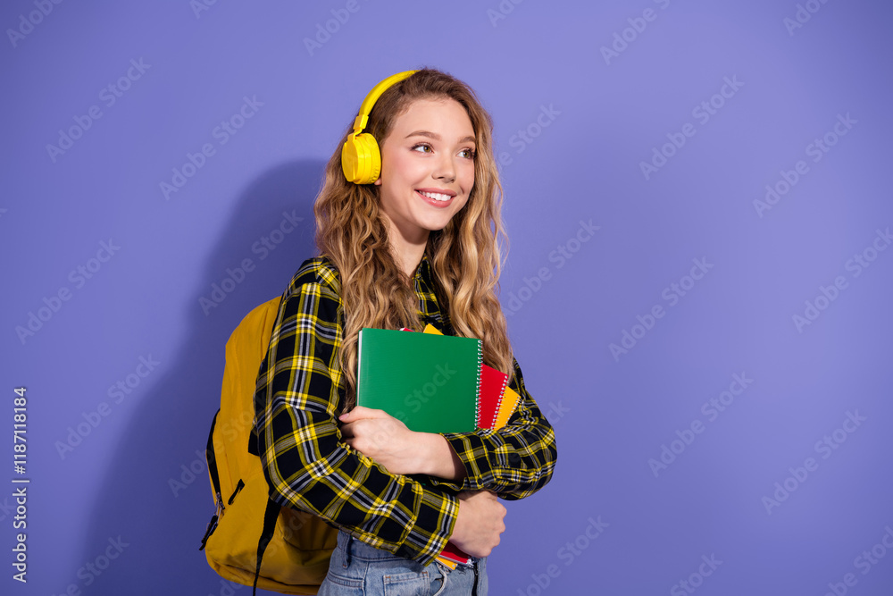 Young cheerful student holding notebooks while wearing headphones on a vibrant purple background Young cheerful student holding notebooks while wearing headphones on a vibrant purple background