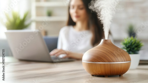 A Wooden Aroma Diffuser Releases Relaxing Mist While a Woman Works on a Laptop in a Cozy Home Office Environment With Green Plants in the Background photo