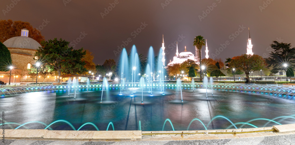 A panoramic nighttime view of a fountain and the Blue Mosque in Istanbul, Turkey.