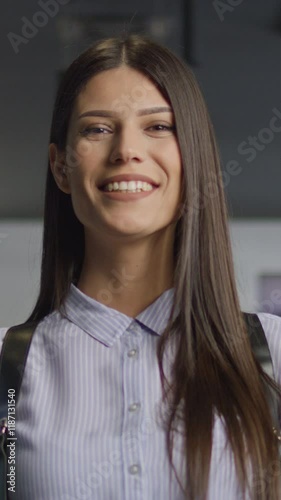 Vertical Screen: Confident young woman nodding her head while smiling, standing in a modern office corridor with glass walls. Concept of agreement, positivity, and professional confidence
