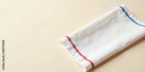 A neatly folded white linen tea towel with red and blue border detailing rests on a pale background