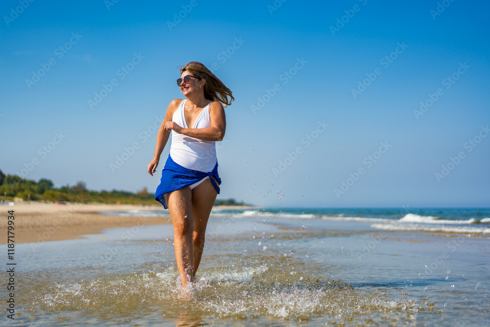 Beautiful middle-aged woman running on sandy beach in summertime. Physical activity on beach. Front view Beautiful middle-aged woman running on sandy beach in summertime. Physical activity on beach. Front view