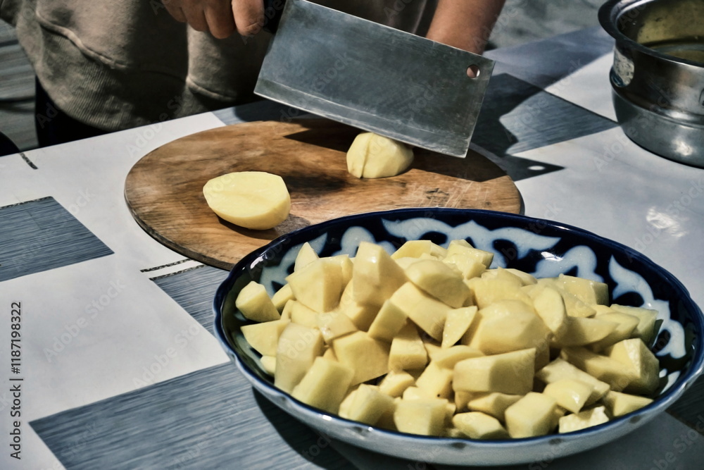 A close-up of the process of cutting potatoes on a wooden board. In the center of the frame, there's a knife and a potato, with a bowl of sliced potatoes in the foreground. A close-up of the process of cutting potatoes on a wooden board. In the center of the frame, there's a knife and a potato, with a bowl of sliced potatoes in the foreground.