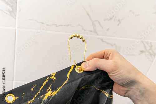 Man attaches golden rings or hooks to black bathroom curtain photo