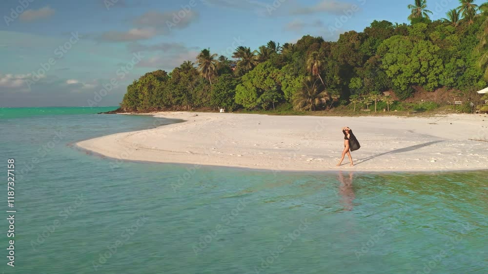 Young woman strolls on a sunny beach in french polynesia, capturing the tranquil paradise with a drone
