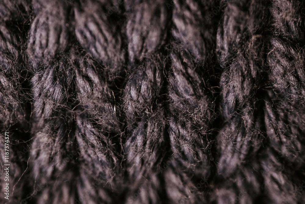 A detailed macro view of dark knitted fabric, showcasing the rich texture and thick yarn weave. The image emphasizes the material's soft and cozy appearance. A detailed macro view of dark knitted fabric, showcasing the rich texture and thick yarn weave. The image emphasizes the material's soft and cozy appearance.