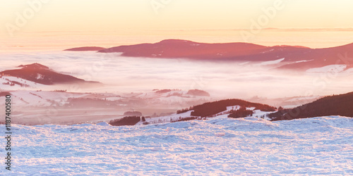 Fototapeta Naklejka Na Ścianę i Meble -  Eastern Sudetes, view of mountain range with thick fog in valley from peak from hiking trail during winter hike in mountains, viewpoint of wide winter landscape in mountains at orange sunset.