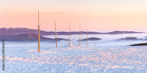 Fototapeta Naklejka Na Ścianę i Meble -  Eastern Sudetes, view of mountain range with thick fog in valley from peak from hiking trail during winter hike in mountains, viewpoint of wide winter landscape in mountains at orange sunset.