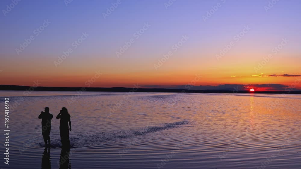 Silhouettes of two people walking on a tranquil lake during a sunset with orange and purple hues. Perfect for nature, serenity, and romance-themed.
Silhouettes of two people walking on a tranquil lake during a sunset with orange and purple hues. Perfect for nature, serenity, and romance-themed.