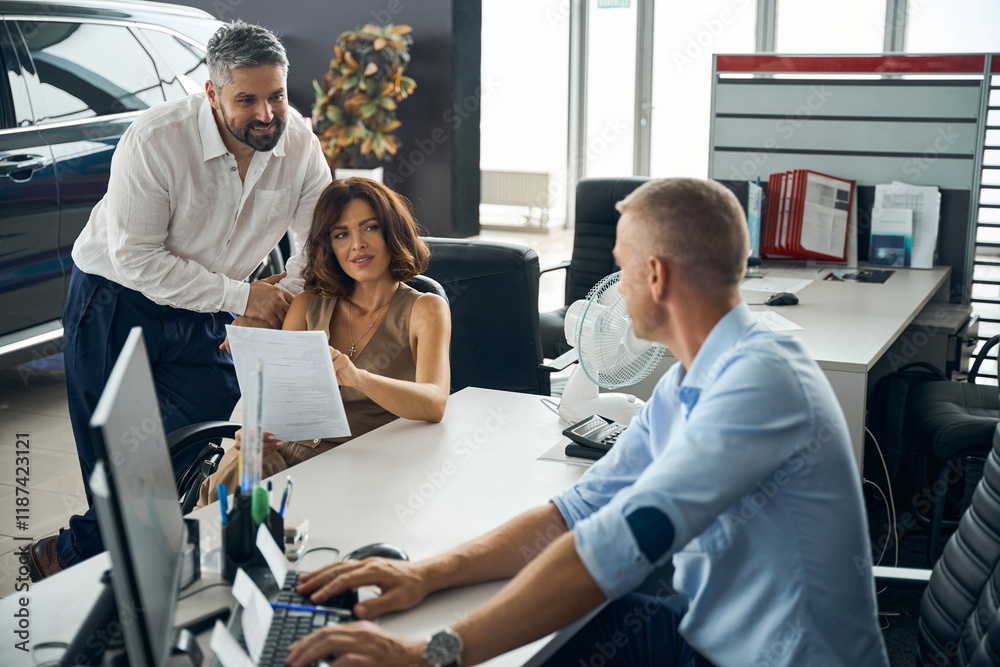 Obraz premium Happy couple reading documents, talking with salesman manager at car salon