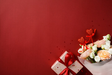 Valentines Day background with a bouquet of roses, a gift box wrapped in white paper with a red ribbon, and red glitter hearts on a red backdrop. Perfect for romantic and festive themes