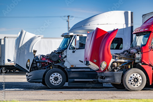 Broken big rig semi trucks with open hoods standing on the industrial parking lot waiting for repair and maintenance specialist