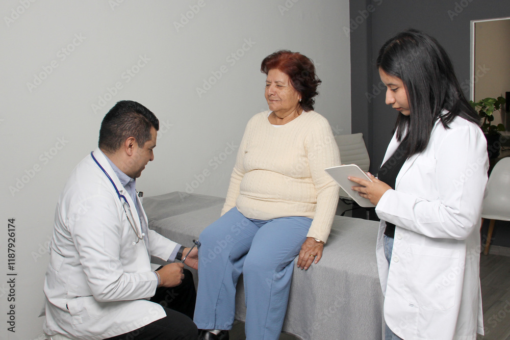 Fototapeta premium Male orthopedic doctor evaluates the reflexes of his patient's legs with the help of his brunette Latina practitioner in the office