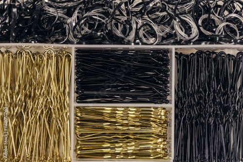 Black and golden hairpins of different sizes and hair scrunchie on plastic box, flat lay, close-up. photo