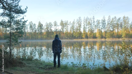 Hiker admires colorful autumn forest reflecting in calm lake