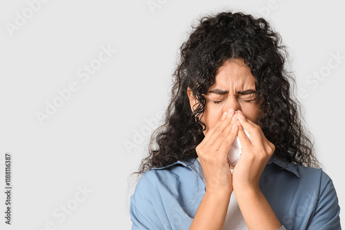 Young African-American woman sneezing in handkerchief on white background. Allergy concept